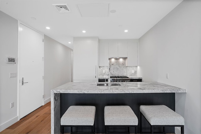 kitchen with visible vents, light countertops, white cabinets, a kitchen bar, and backsplash