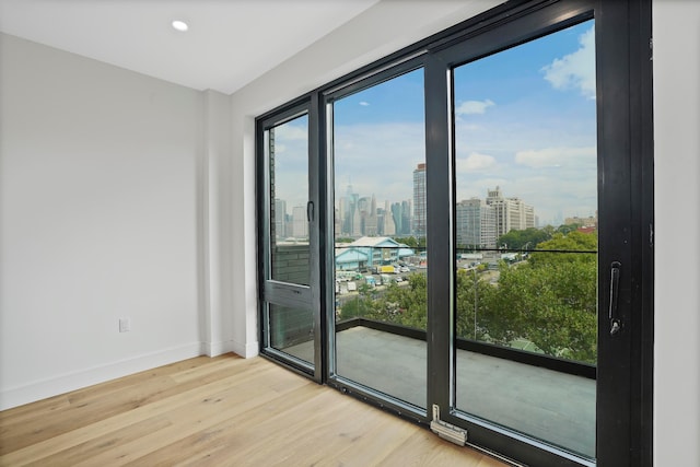 unfurnished room with a view of city, recessed lighting, baseboards, and light wood-type flooring