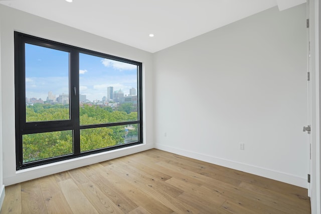 empty room with a city view, plenty of natural light, baseboards, and light wood-type flooring