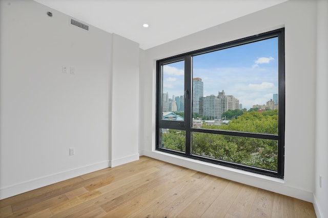 spare room with a wealth of natural light, a city view, visible vents, and hardwood / wood-style floors