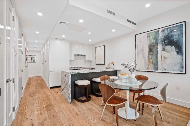 kitchen with sink, a breakfast bar area, white cabinetry, light wood-type flooring, and kitchen peninsula