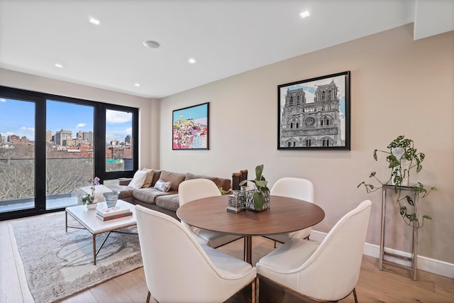 dining room featuring light wood finished floors, recessed lighting, a view of city, and baseboards