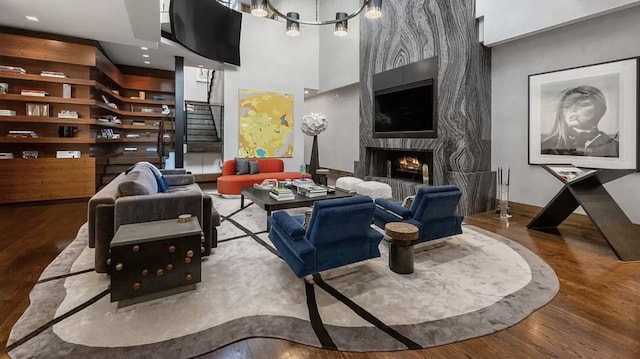 living room featuring a towering ceiling, a chandelier, a fireplace, and hardwood / wood-style flooring