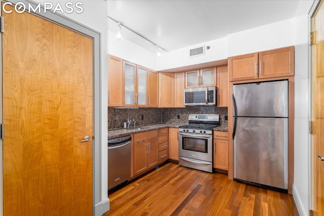 kitchen with tasteful backsplash, dark hardwood / wood-style floors, dark stone countertops, sink, and appliances with stainless steel finishes