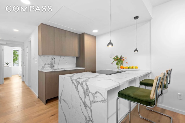 kitchen featuring a sink, light wood-style flooring, a peninsula, light stone countertops, and decorative backsplash