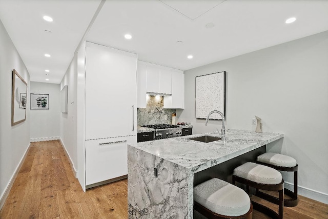 kitchen featuring kitchen peninsula, backsplash, white cabinets, light hardwood / wood-style flooring, and sink