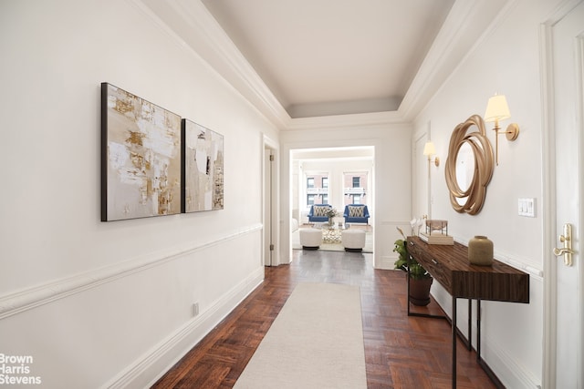 corridor with baseboards, a raised ceiling, and crown molding