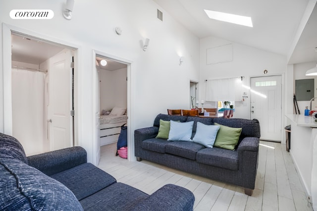 living room with high vaulted ceiling, a skylight, light hardwood / wood-style floors, and electric panel