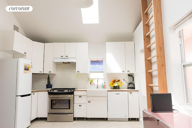 kitchen featuring sink, white appliances, white cabinetry, a skylight, and tasteful backsplash