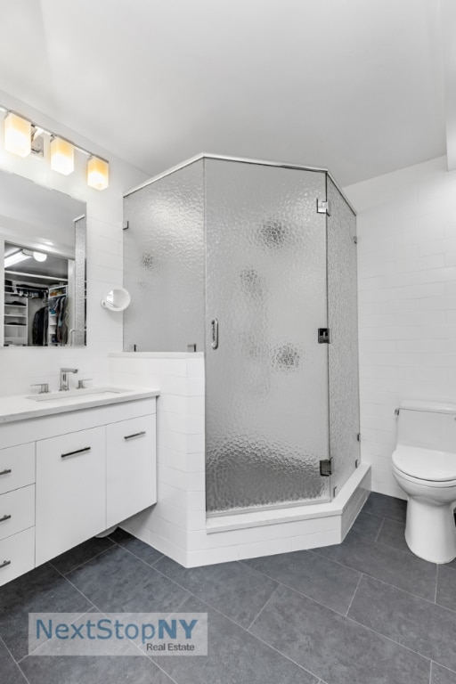 bathroom featuring tile patterned flooring, toilet, a shower with door, and vanity