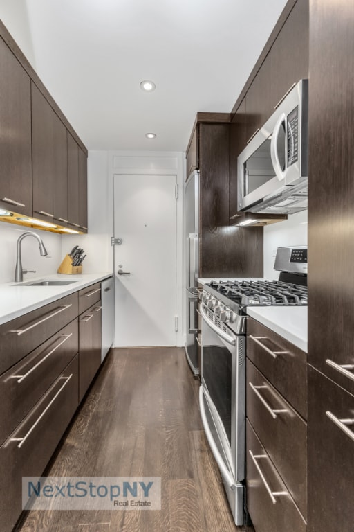 kitchen with sink, appliances with stainless steel finishes, dark hardwood / wood-style flooring, and dark brown cabinets