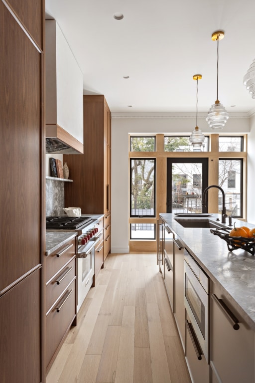 kitchen with pendant lighting, appliances with stainless steel finishes, white cabinets, sink, and ornamental molding