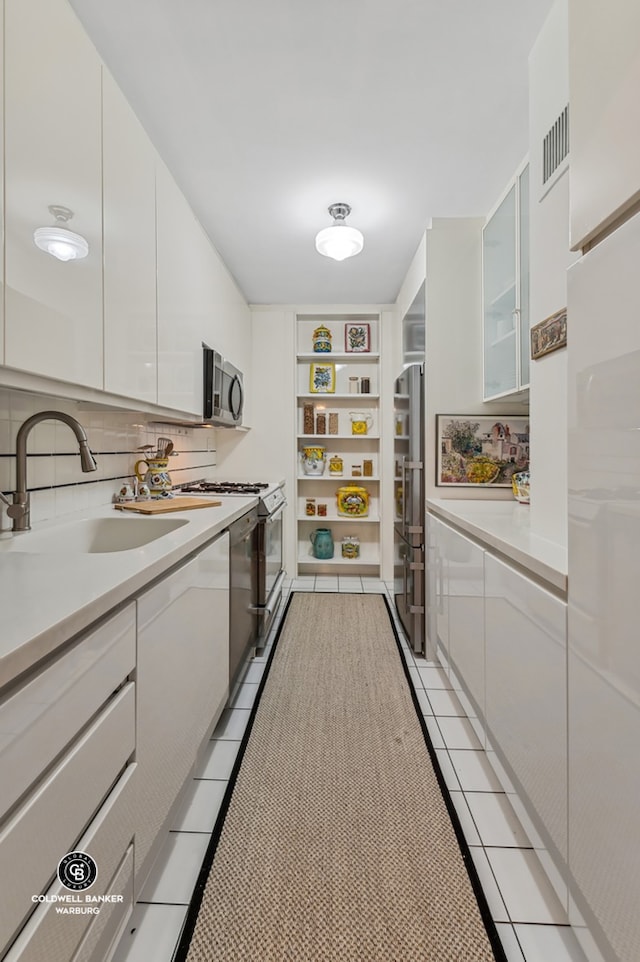 kitchen featuring stainless steel microwave, white cabinets, a sink, and light tile patterned flooring