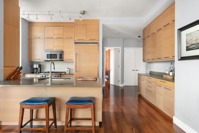 kitchen with paneled built in fridge, stainless steel microwave, a kitchen breakfast bar, and dark wood-style flooring