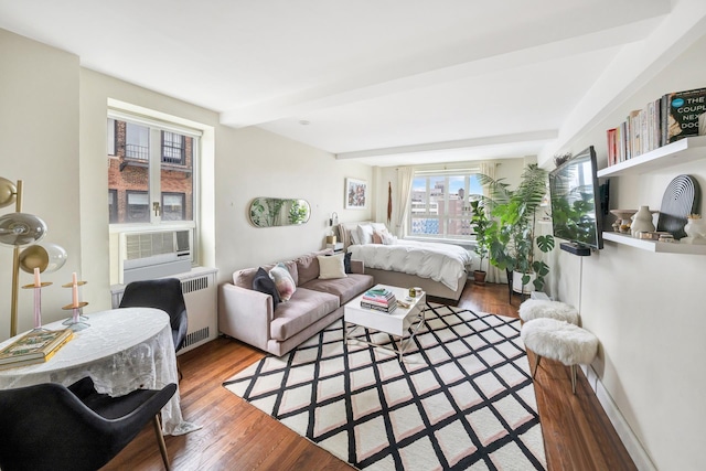 bedroom with cooling unit, beam ceiling, wood finished floors, and radiator heating unit