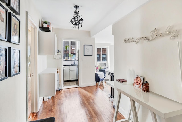 corridor with a notable chandelier, light wood-style flooring, and baseboards