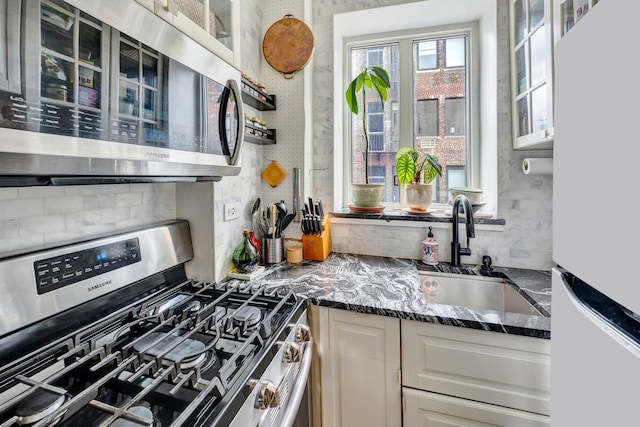 kitchen featuring appliances with stainless steel finishes, glass insert cabinets, a sink, and white cabinetry