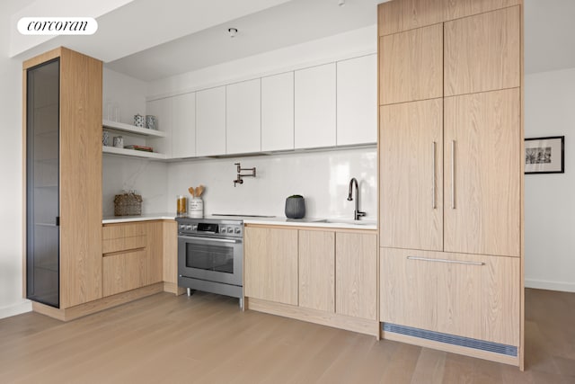 kitchen with stainless steel range, decorative backsplash, light brown cabinetry, light hardwood / wood-style flooring, and sink