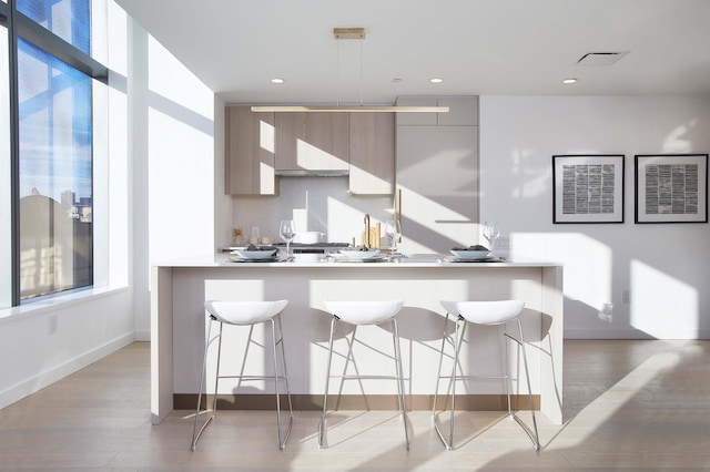 kitchen with a kitchen bar, light countertops, light wood-style floors, modern cabinets, and baseboards