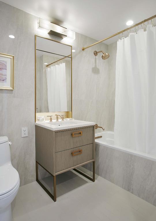 full bathroom featuring toilet, shower / tub combo, tile walls, and vanity