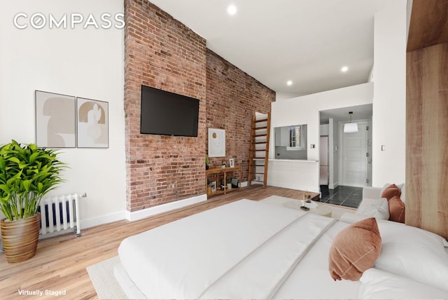 bedroom featuring radiator heating unit, ensuite bathroom, wood-type flooring, and brick wall