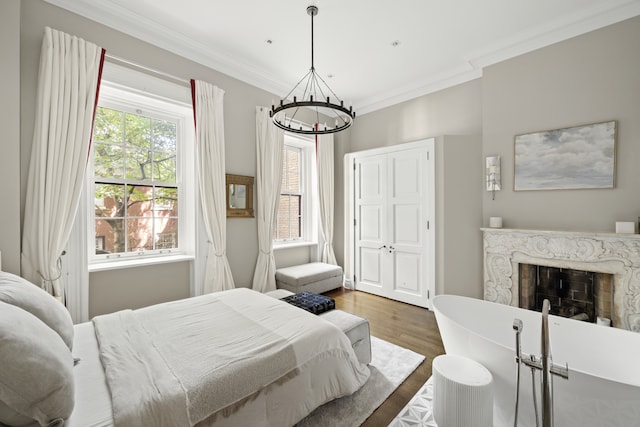 bedroom with crown molding, a premium fireplace, wood finished floors, a closet, and a notable chandelier