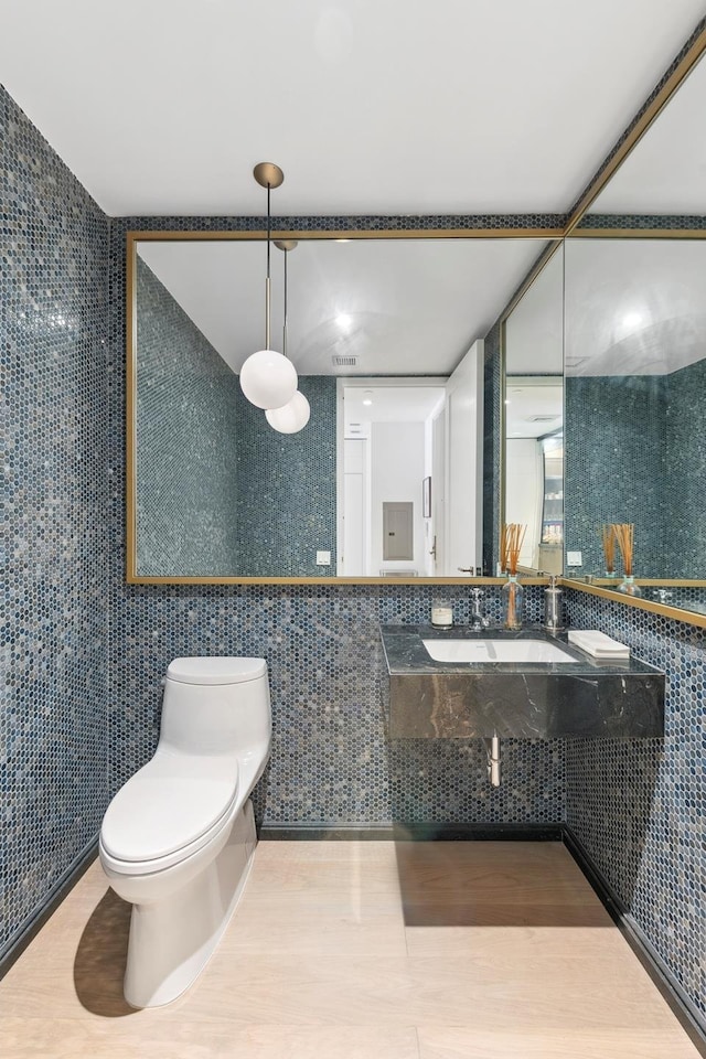 bathroom with tile walls, toilet, wood finished floors, and a sink