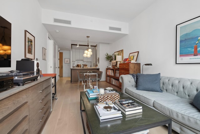living room with an inviting chandelier, light wood-type flooring, and visible vents