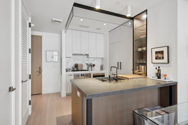 kitchen with visible vents, modern cabinets, light wood-type flooring, white cabinetry, and a sink