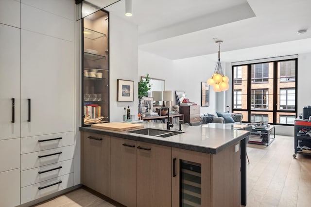 kitchen featuring hanging light fixtures, a sink, beverage cooler, open floor plan, and light wood-style flooring
