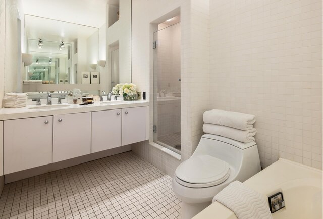 bathroom with toilet, vanity, tile walls, tile patterned floors, and an enclosed shower