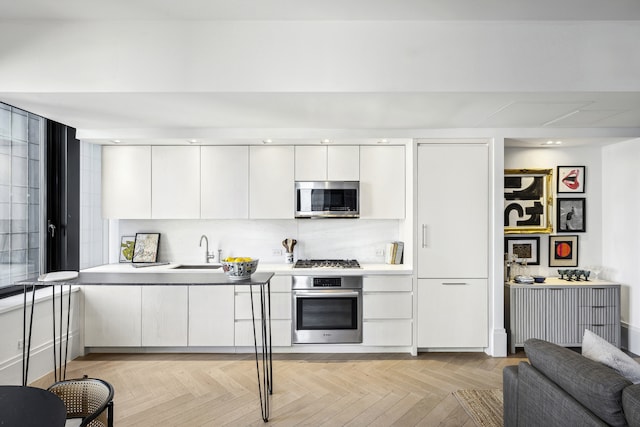 kitchen with modern cabinets, appliances with stainless steel finishes, light countertops, white cabinetry, and a sink