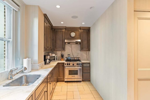 kitchen featuring high end stove, sink, decorative backsplash, light tile patterned floors, and light stone countertops