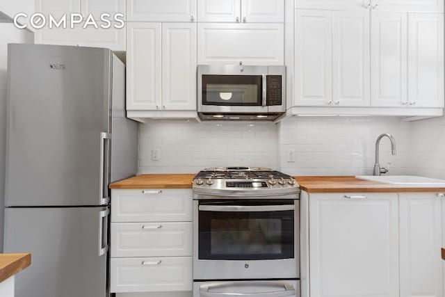 kitchen with wood counters, sink, stainless steel appliances, and white cabinets