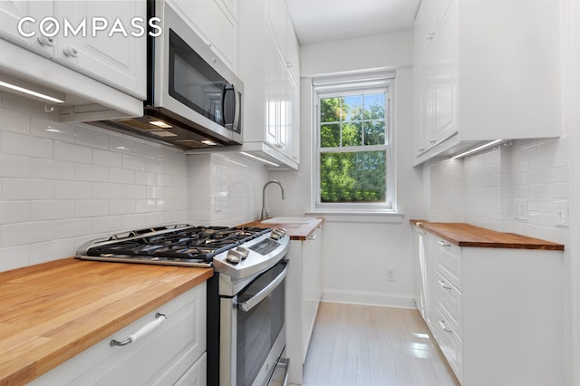 kitchen featuring tasteful backsplash, white cabinets, appliances with stainless steel finishes, wooden counters, and a sink