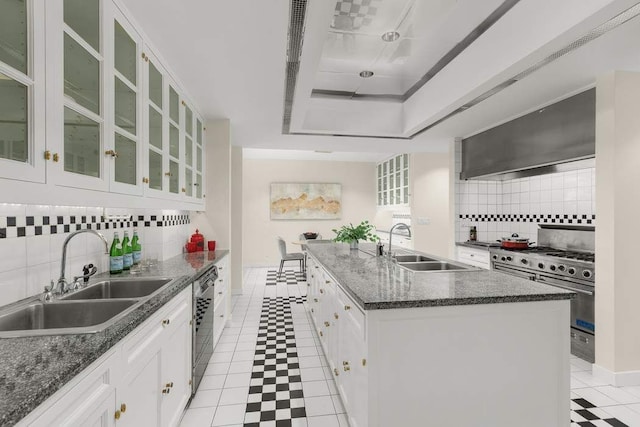 kitchen with sink, wall chimney range hood, white cabinets, and a kitchen island with sink