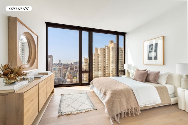 bedroom featuring a view of city, visible vents, expansive windows, and light wood-type flooring