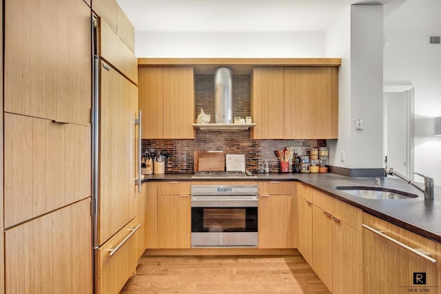 kitchen with appliances with stainless steel finishes, dark countertops, a sink, and wall chimney range hood