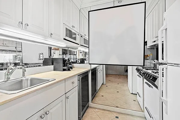 kitchen with sink, white appliances, light tile patterned flooring, white cabinets, and beverage cooler