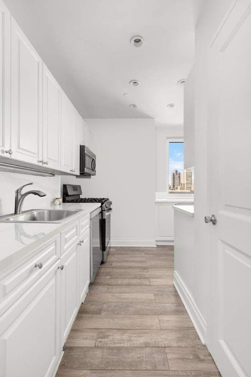 kitchen with light wood-type flooring, sink, stainless steel appliances, and white cabinetry