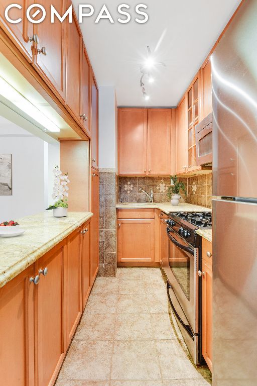 kitchen featuring sink, stainless steel gas range, backsplash, fridge, and light stone countertops