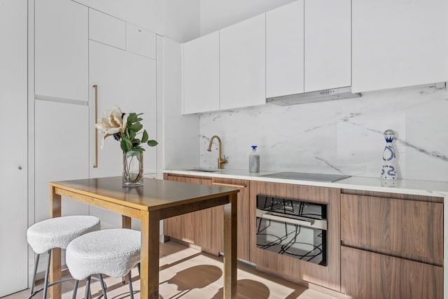 kitchen featuring decorative backsplash, white cabinets, a sink, under cabinet range hood, and black appliances