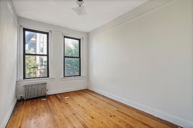 empty room featuring light wood-type flooring, baseboards, and radiator