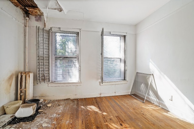 empty room featuring a healthy amount of sunlight, radiator, and wood-type flooring