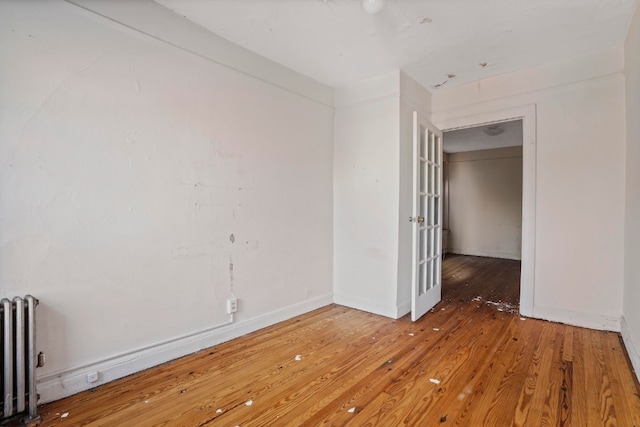 spare room with radiator heating unit, baseboards, and wood-type flooring