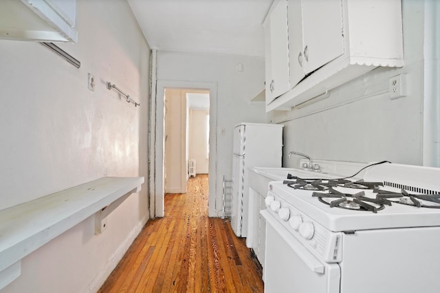 kitchen with radiator heating unit, hardwood / wood-style floors, white cabinets, and white appliances