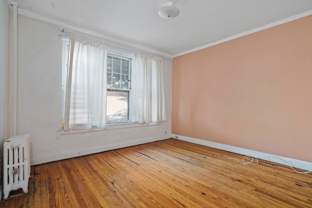 spare room featuring hardwood / wood-style floors, radiator heating unit, baseboards, and ornamental molding