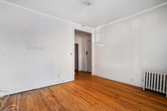 unfurnished room with crown molding, radiator heating unit, baseboards, and wood finished floors