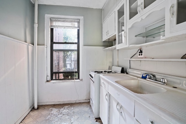 interior space with white gas range, sink, and white cabinets