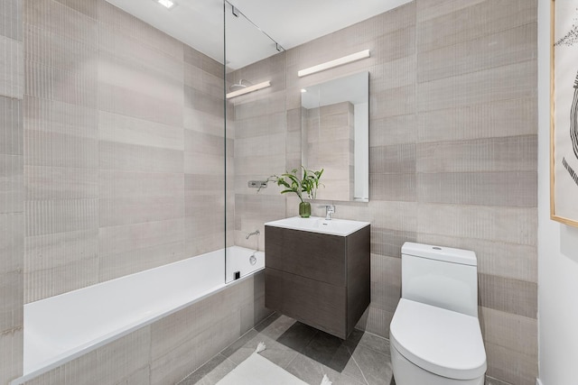 bathroom with toilet, tile patterned flooring, tiled shower / bath, vanity, and tile walls